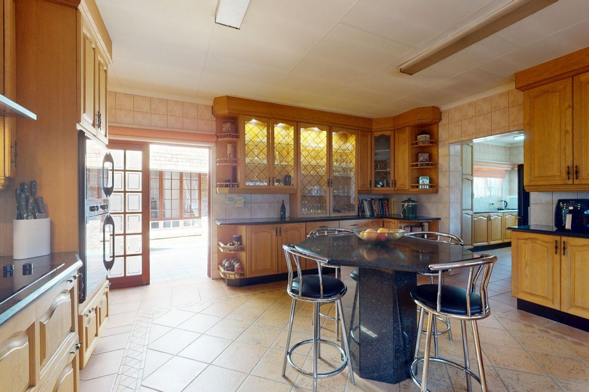 Spacious kitchen featuring warm-toned wooden cabinetry, granite countertops, integrated display cabinets, and direct access to an outdoor patio area.
