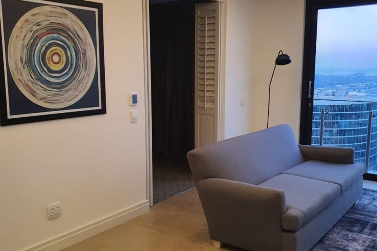 Modern living room featuring recessed cove lighting, large format floor tiles, and a sliding glass door leading to a balcony with city views.