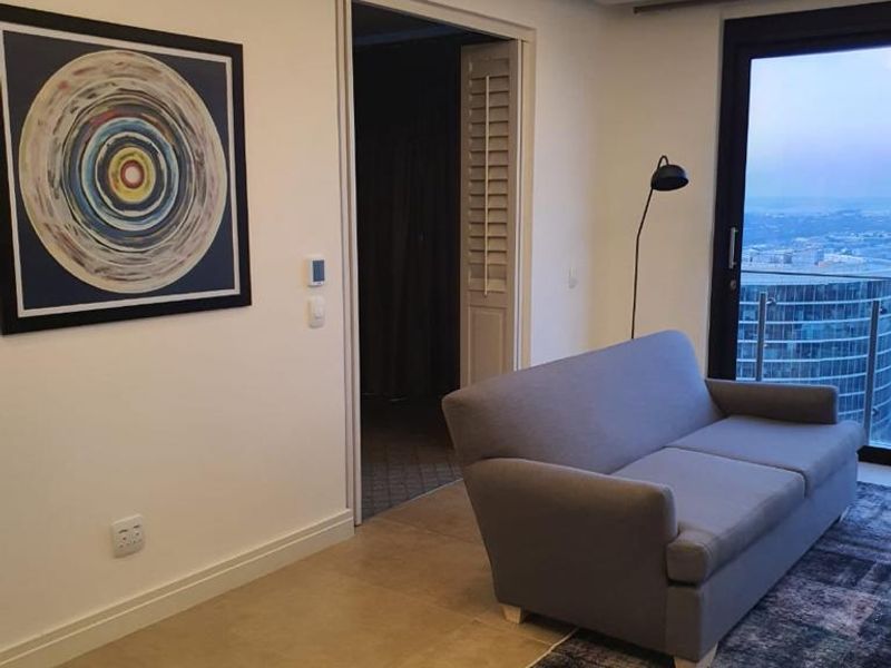 Modern living room featuring recessed cove lighting, large format floor tiles, and a sliding glass door leading to a balcony with city views.