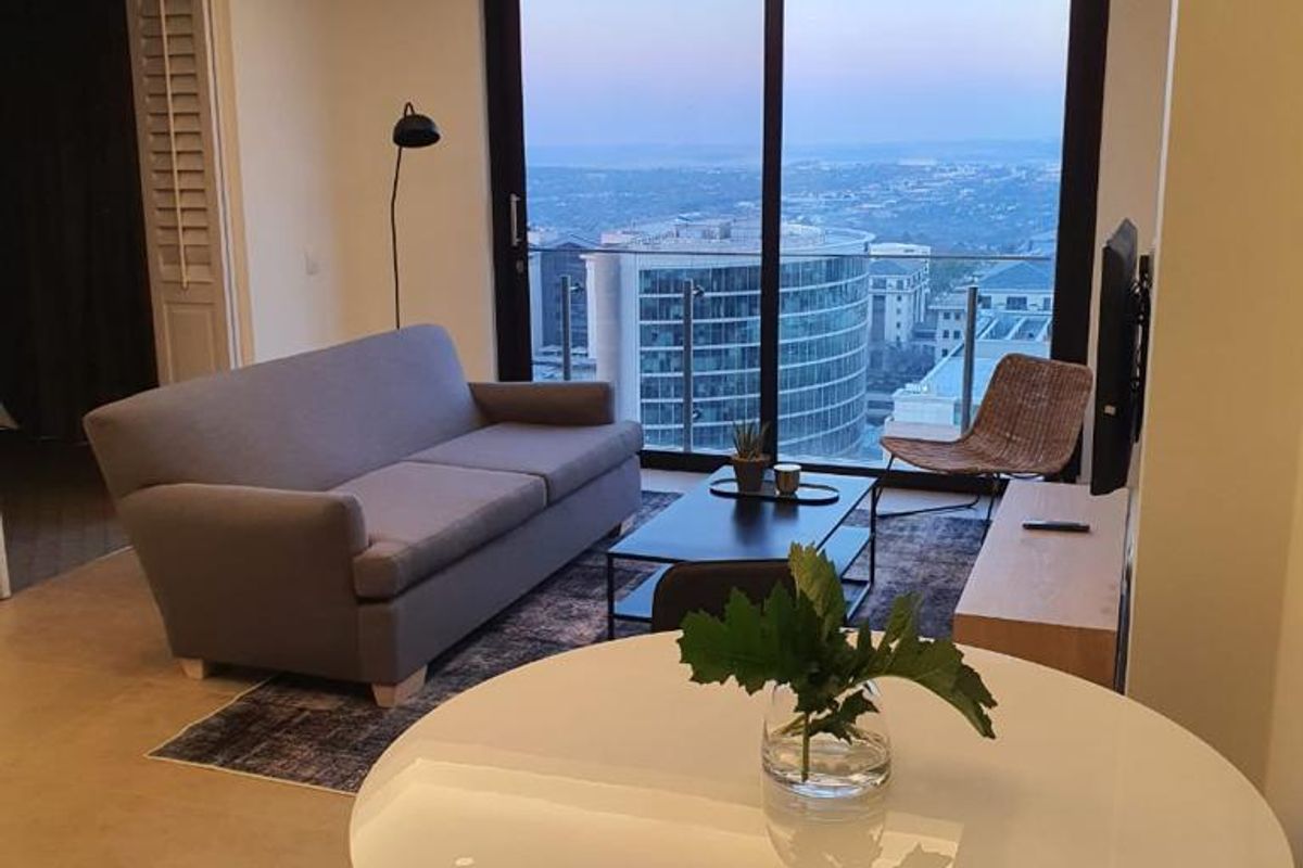 Modern open-plan living area featuring recessed ceiling lighting, tiled floors, and large sliding glass doors opening to a balcony with city views.