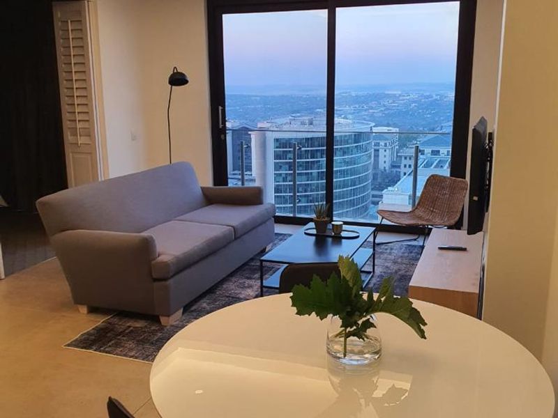 Modern open-plan living area featuring recessed ceiling lighting, tiled floors, and large sliding glass doors opening to a balcony with city views.