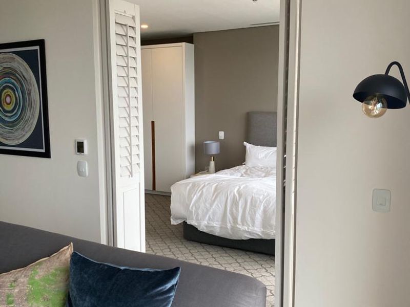 A view into a bedroom featuring a built-in wardrobe and shutter-style door, viewed from an adjacent living space.