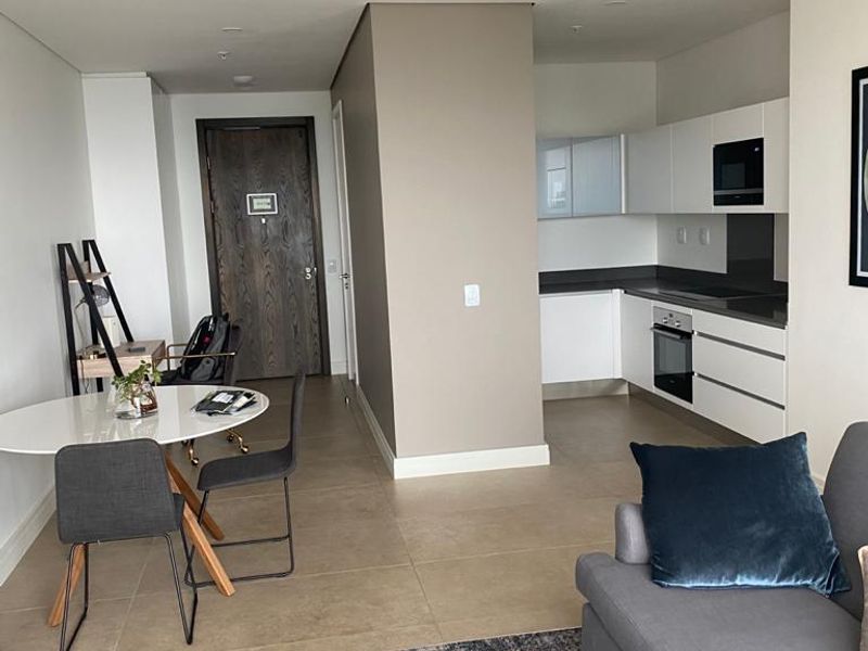 Modern open-plan apartment featuring a sleek kitchen with integrated appliances, ducted air conditioning, and neutral tiled flooring throughout the living and dining area.