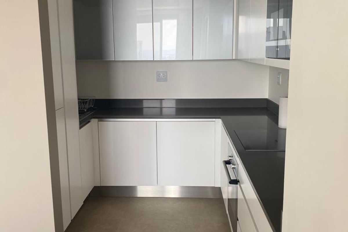 A modern, minimalist kitchen featuring sleek white cabinetry, dark stone countertops, and integrated appliances in a clean, neutral-toned space.