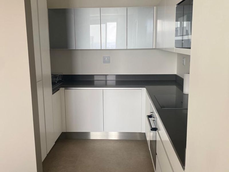A modern, minimalist kitchen featuring sleek white cabinetry, dark stone countertops, and integrated appliances in a clean, neutral-toned space.