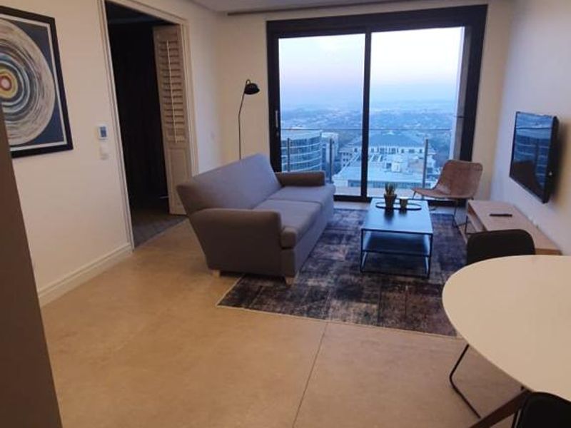 Modern living room featuring large format floor tiles, recessed ceiling lighting, and sliding glass doors opening to a balcony with expansive views.