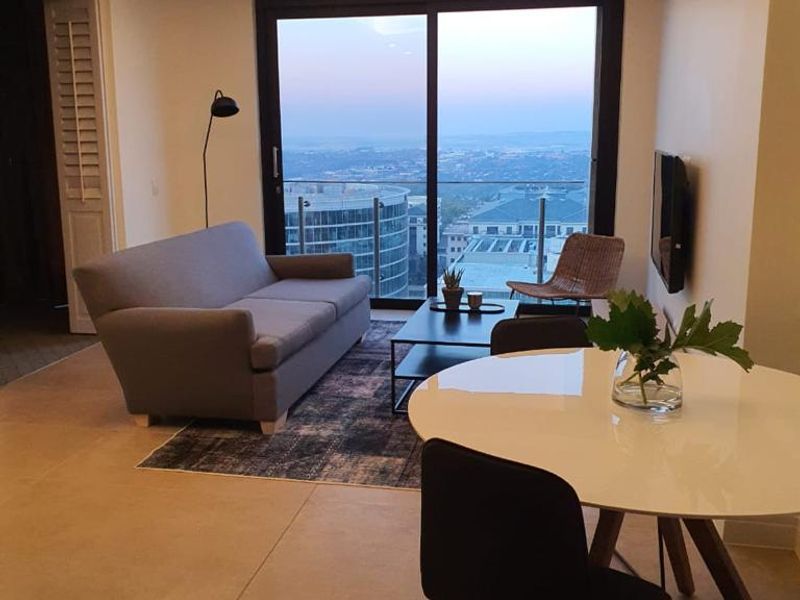 Modern open-plan living and dining area featuring large format floor tiles, recessed ceiling lighting, and a sliding glass door leading to a balcony with views.