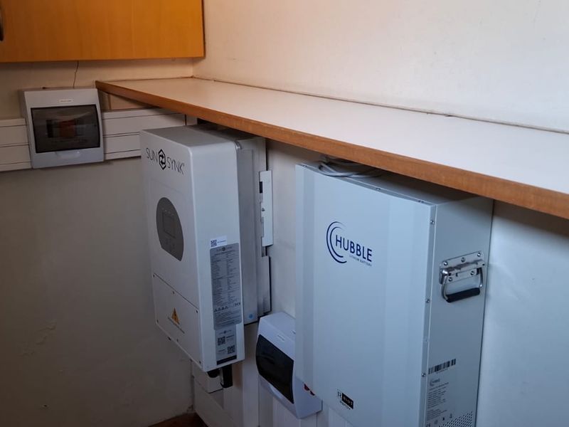 Utility area featuring a wall-mounted solar inverter, lithium battery storage system, and electrical distribution board with integrated shelving.