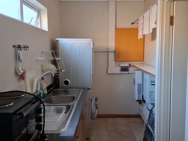 Functional laundry area featuring a stainless steel sink, built-in cabinetry, and wall-mounted gas geyser units.