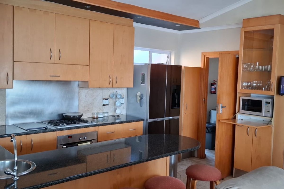 A functional kitchen featuring light wood cabinetry, granite countertops, a gas hob, and a breakfast bar, offering ample storage and workspace.