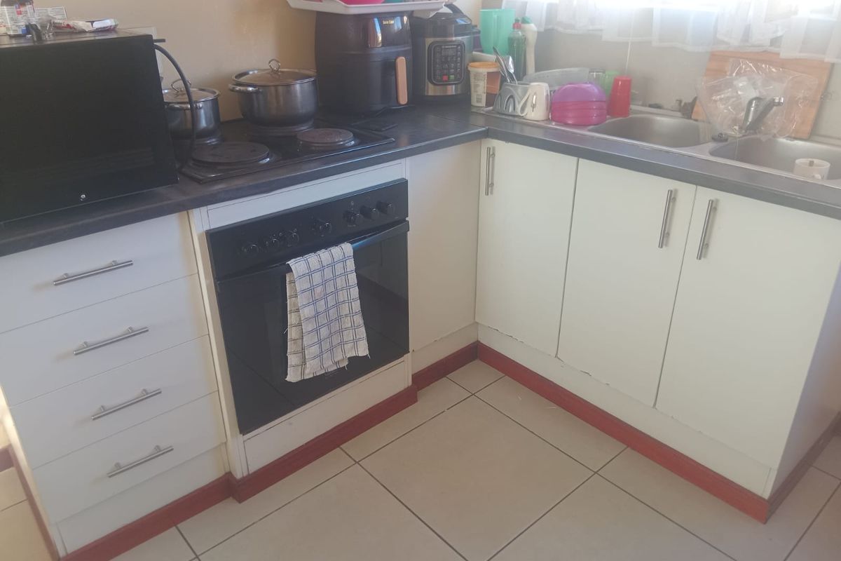 A functional kitchen featuring built-in oven, electric hob, stainless steel sink, and white base cabinetry with tiled flooring.