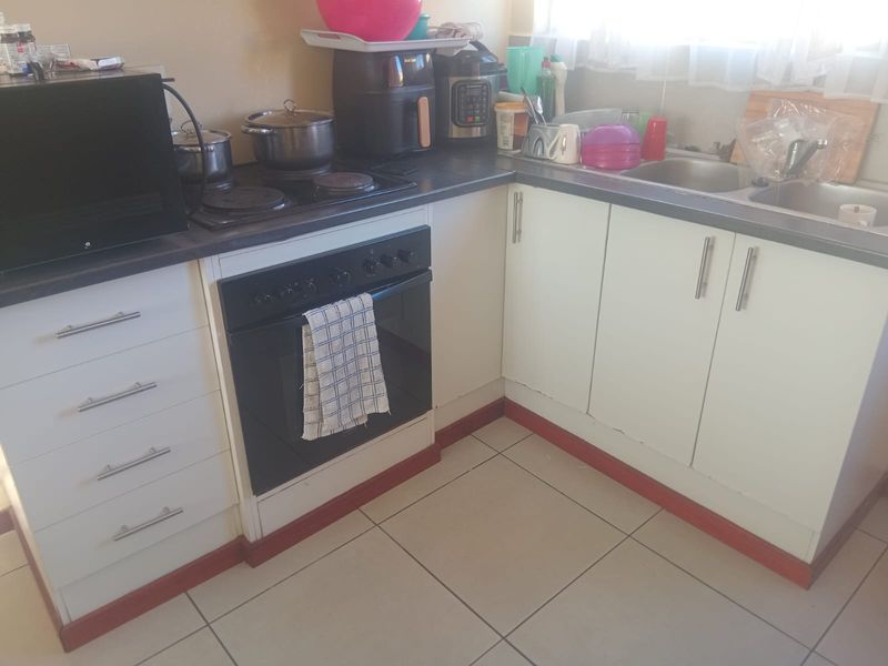 A functional kitchen featuring built-in oven, electric hob, stainless steel sink, and white base cabinetry with tiled flooring.
