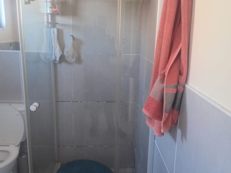 A functional bathroom featuring a glass-enclosed shower and a standard toilet with neutral wall and floor tiling.