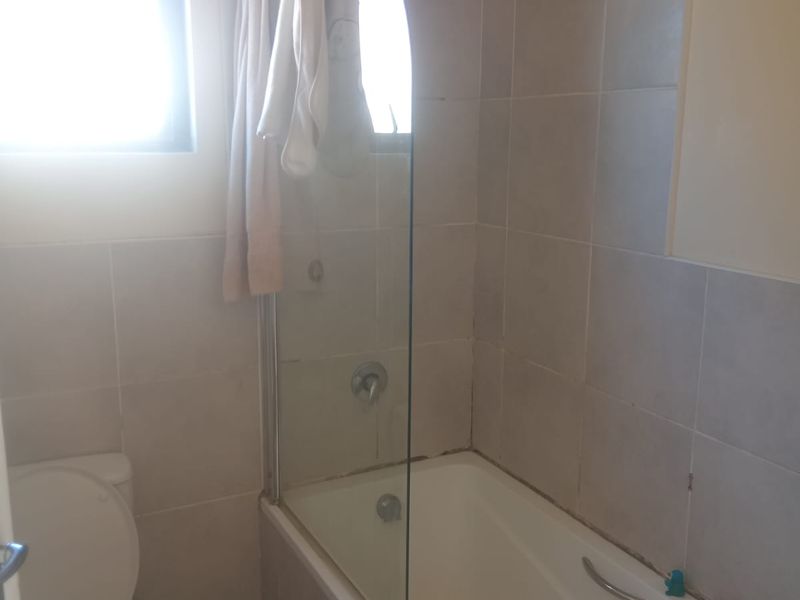 A functional bathroom featuring a bathtub with a glass shower screen, tiled walls, and a standard toilet.
