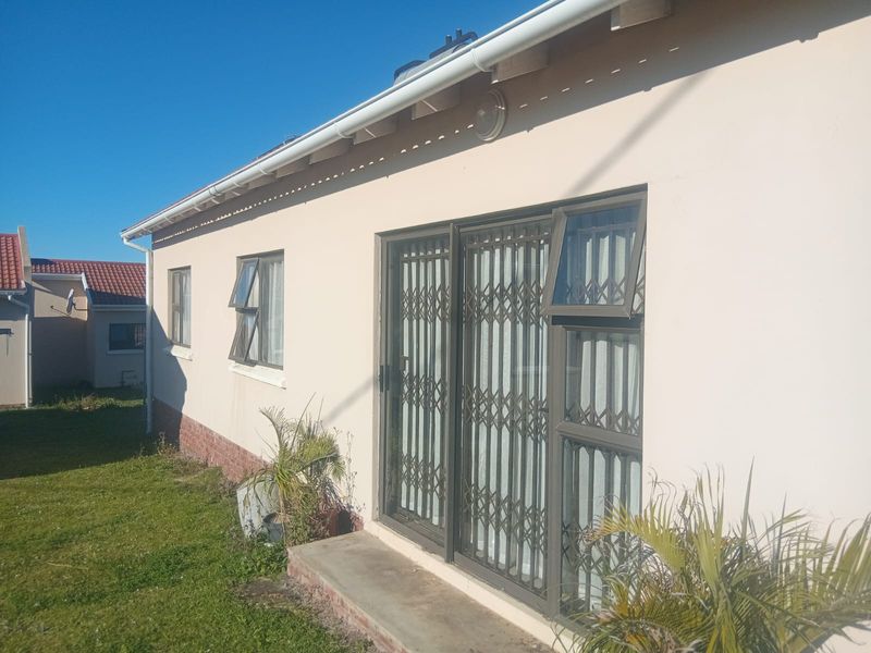 Rear exterior view of the townhouse featuring a sliding glass door with security gate, top-hung windows, and a small concrete threshold.