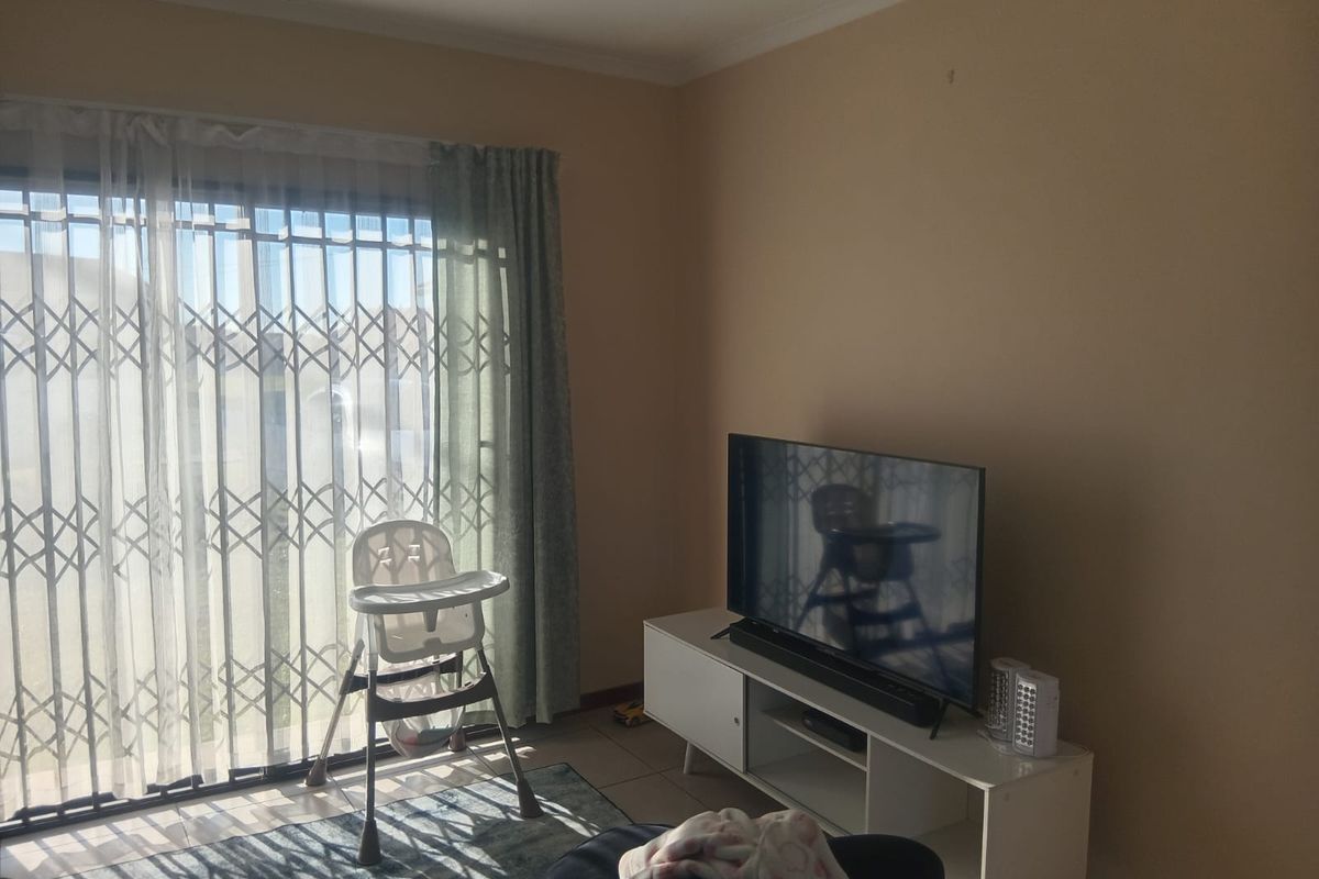 A living room featuring tiled flooring, a sliding door with a security gate, and neutral wall finishes.