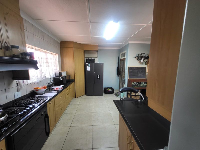 A functional kitchen featuring wooden cabinetry, gas hob, extractor fan, and tiled flooring, offering a practical layout with ample counter space.