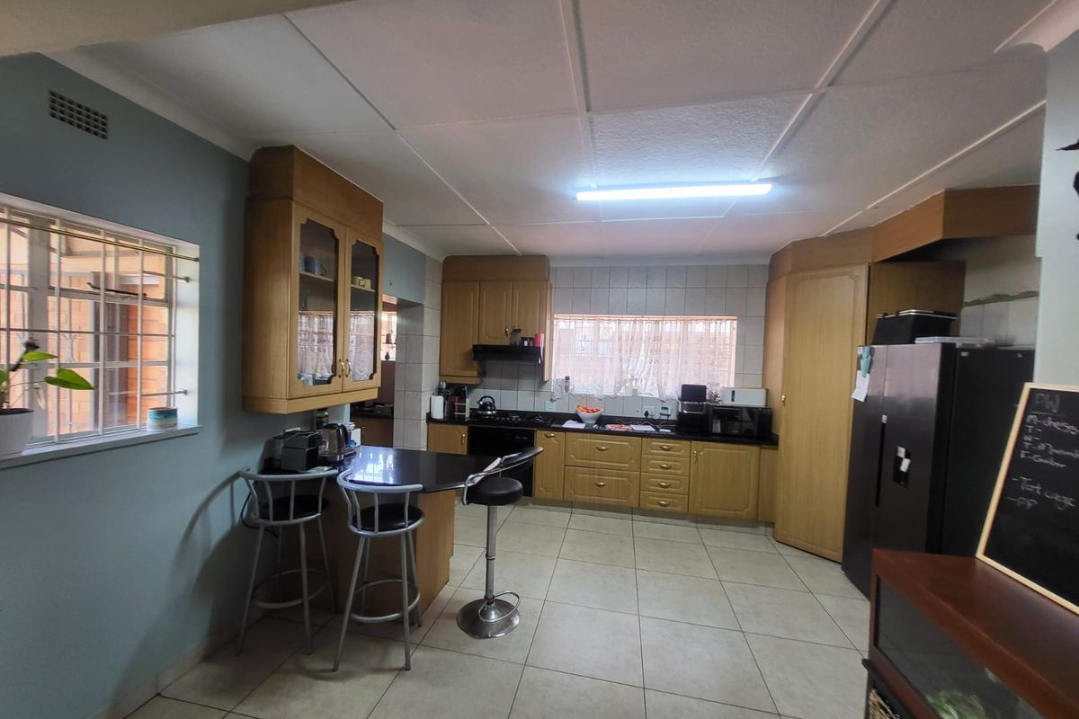 A functional kitchen featuring wooden cabinetry, laminate countertops, a built-in hob with extractor fan, and tiled flooring.