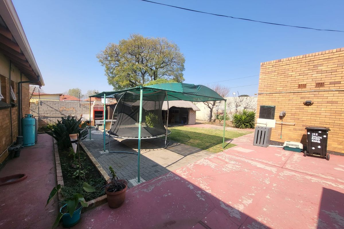 Rear exterior area featuring a paved section, painted concrete patio, built-in braai, and a thatched lapa structure in the garden.