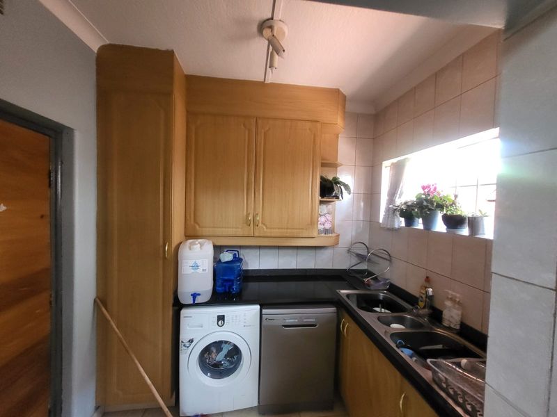 A functional laundry area featuring built-in wooden cabinetry, a double bowl sink, and tiled splashbacks with space for under-counter appliances.