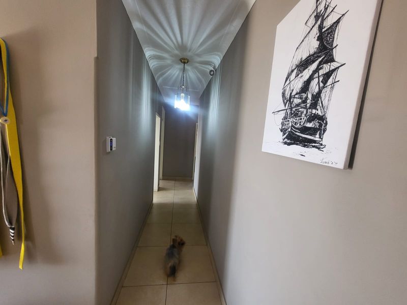 A clean and well-maintained interior hallway featuring neutral wall tones, tiled flooring, and a central pendant light fixture.