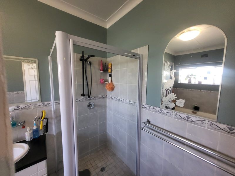 A functional bathroom featuring a shower enclosure, vanity basin, and decorative wall mirror with tiled splashback finishes.