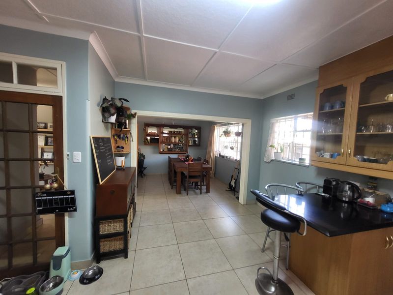 Open-plan living and dining area featuring tiled flooring, built-in wooden cabinetry, and a breakfast bar, creating a functional and connected living space.