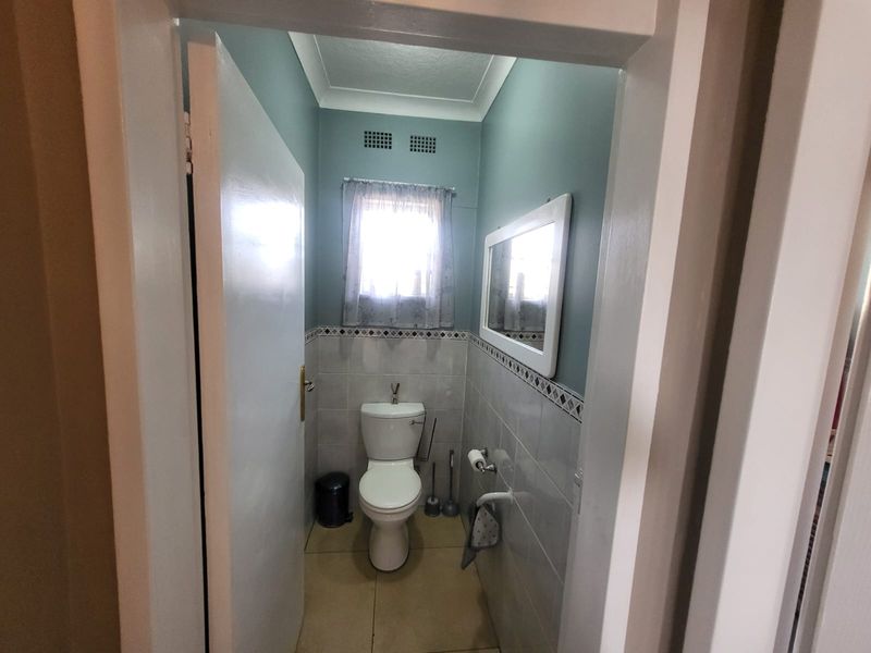 A compact bathroom featuring tiled walls with decorative border, tiled flooring, and a standard toilet suite.