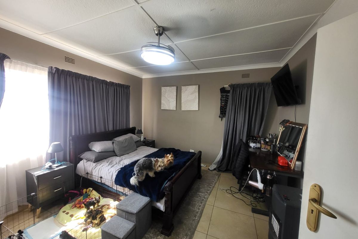 A functional bedroom featuring tiled flooring, a central ceiling fan, and neutral wall tones, providing a comfortable and practical living space.