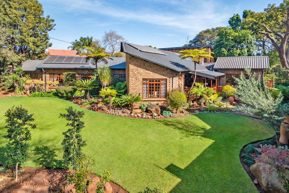 A well-maintained face brick house featuring a pitched metal roof with solar panels, set within a lush, landscaped garden with a covered patio area.