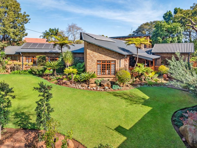 A well-maintained face brick house featuring a pitched metal roof with solar panels, set within a lush, landscaped garden with a covered patio area.