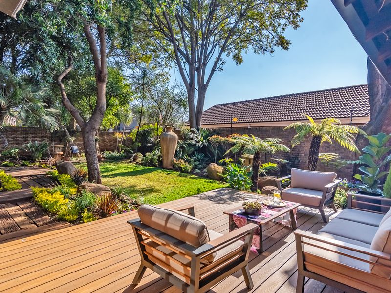 A well-maintained timber deck patio overlooking a lush, landscaped garden with mature trees and a secure brick boundary wall.