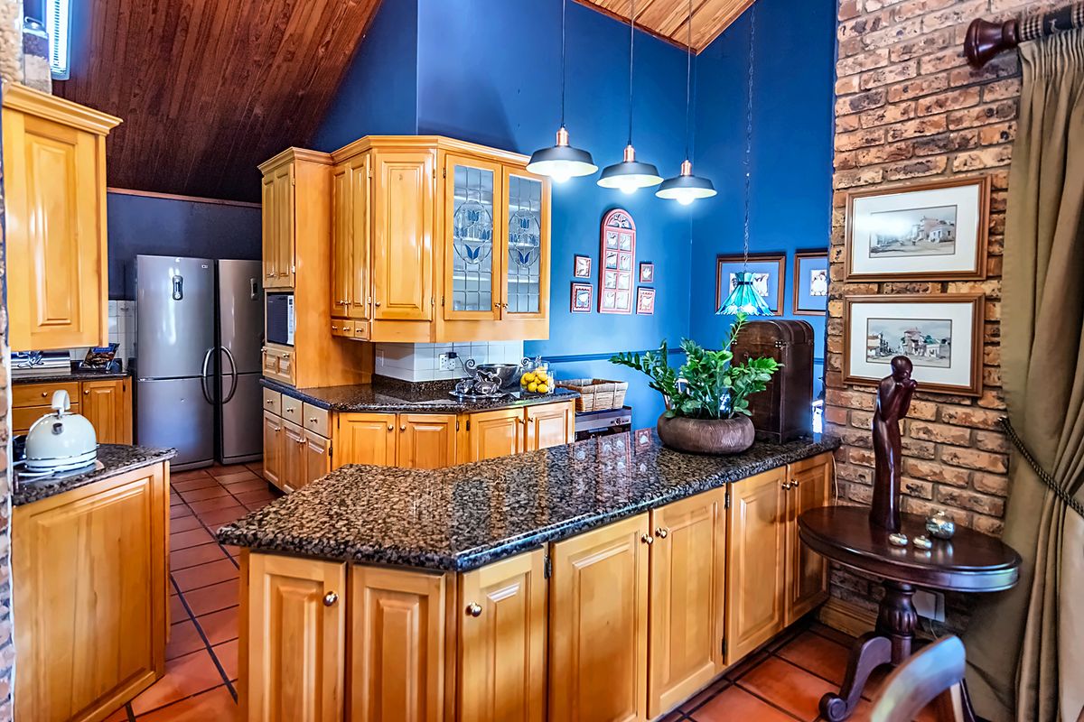 A traditional kitchen featuring timber cabinetry, granite countertops, and an exposed brick feature wall under a vaulted timber ceiling with terracotta flooring.