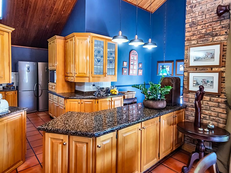 A traditional kitchen featuring timber cabinetry, granite countertops, and an exposed brick feature wall under a vaulted timber ceiling with terracotta flooring.
