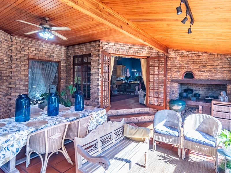 Covered patio featuring exposed timber ceilings, brick walls, and a built-in brick fireplace, providing a rustic outdoor entertainment space with direct access to the home.