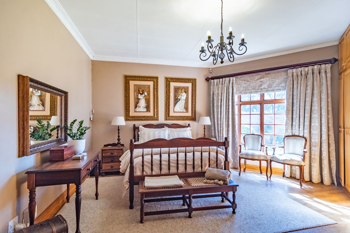 A well-maintained bedroom featuring crown molding, a classic chandelier, and a large built-in wardrobe with natural light from a multi-pane window.