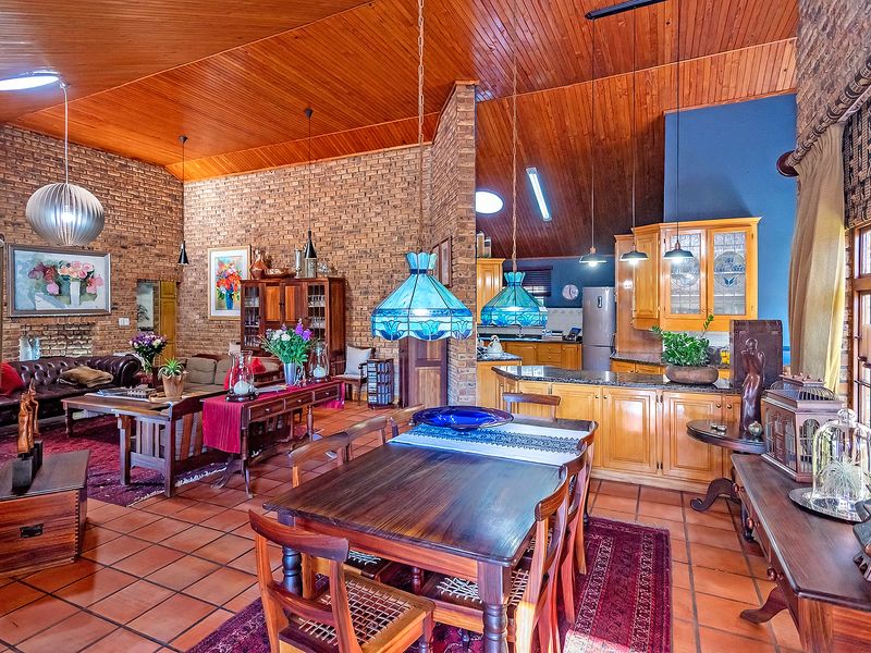 Spacious open-plan living, dining, and kitchen area featuring high timber ceilings, exposed brick walls, and durable terracotta flooring throughout.