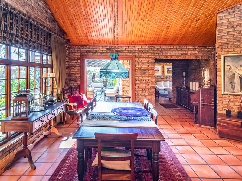 Spacious dining room featuring exposed brick walls, warm timber ceiling, and terracotta flooring, with direct access to an outdoor patio area.