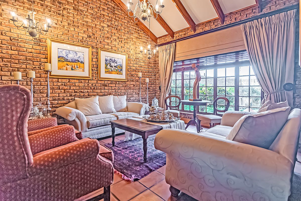 A cozy living room featuring exposed brick walls, vaulted ceilings with timber beams, and large windows that provide ample natural light.