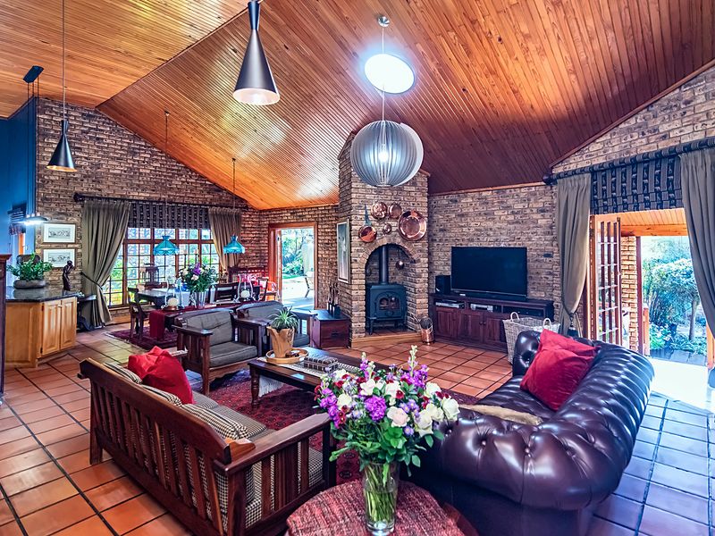 Spacious open-plan living area featuring vaulted timber ceilings, exposed brick walls, terracotta flooring, and a cozy wood-burning fireplace with direct garden access.