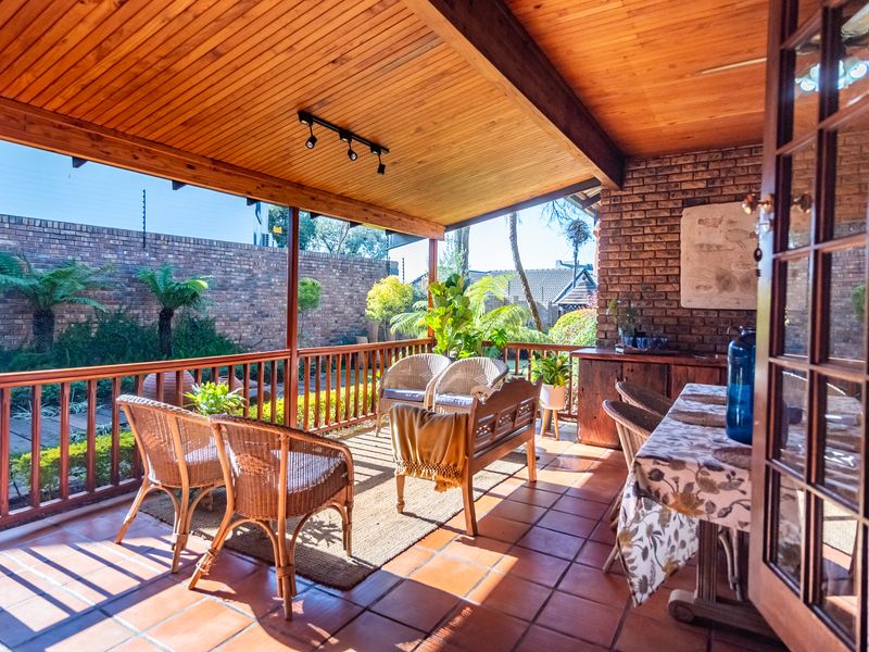 A covered patio featuring a timber-clad ceiling, exposed brick wall, and terracotta floor tiles, providing a comfortable outdoor living space overlooking the garden.