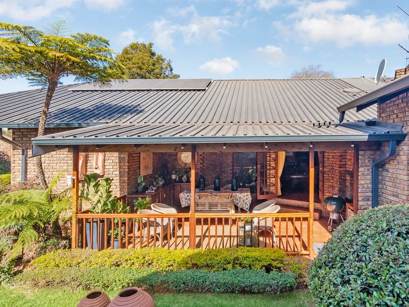 A covered outdoor patio featuring a corrugated metal roof with solar panels, brick walls, and a wooden deck overlooking the garden.