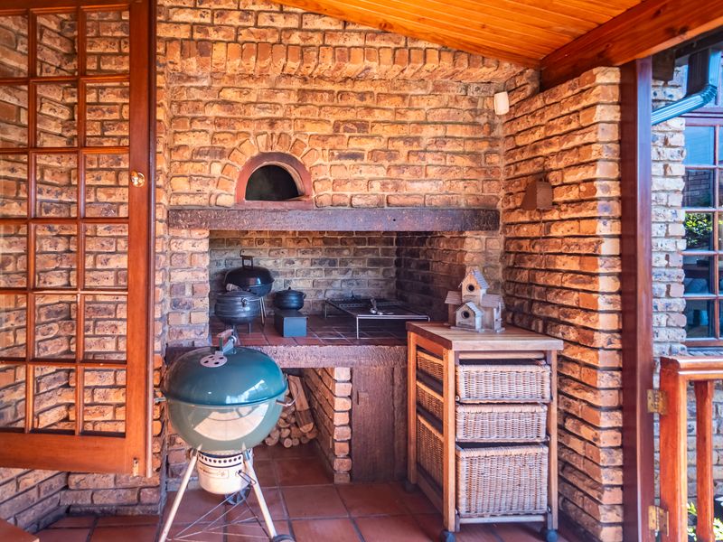 Covered outdoor patio featuring a rustic built-in brick braai and fireplace, timber ceiling, and terracotta flooring, perfect for outdoor entertaining.