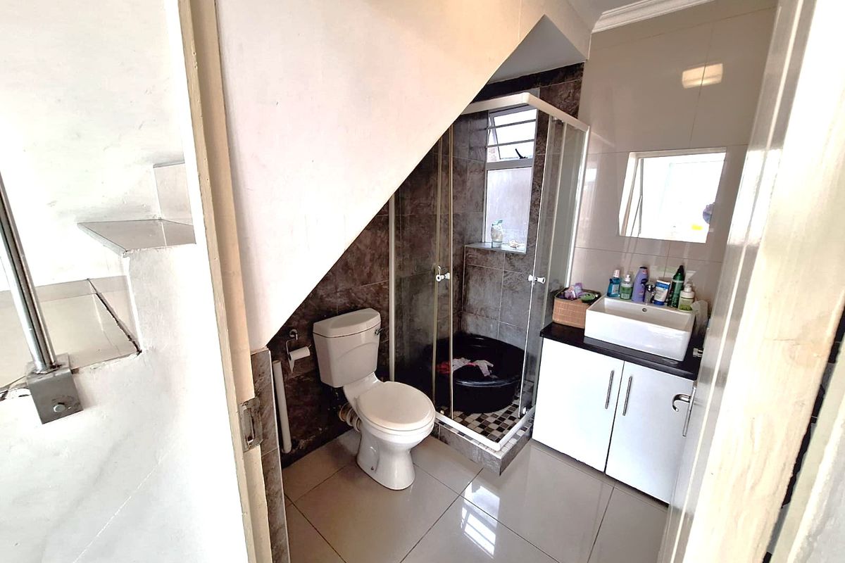 Compact bathroom featuring a shower enclosure, toilet, and vanity cabinet with basin, situated under a staircase with tiled finishes.