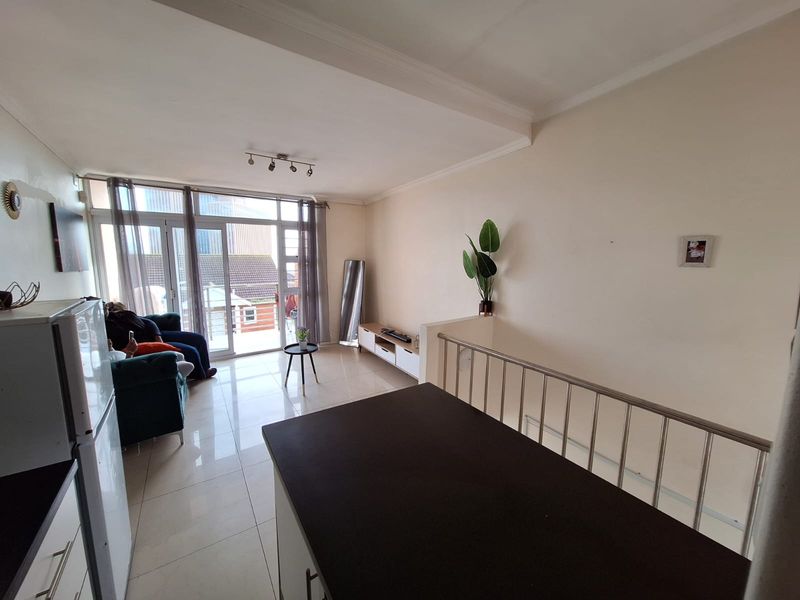 Open-plan living area featuring tiled flooring, a kitchen island, and a stainless steel balustrade, with direct access to a balcony through sliding glass doors.