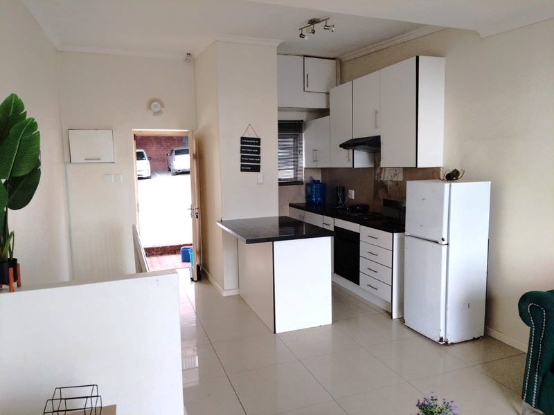 Open-plan kitchen featuring white cabinetry, a breakfast counter, and tiled flooring, with direct access to the exterior entrance.