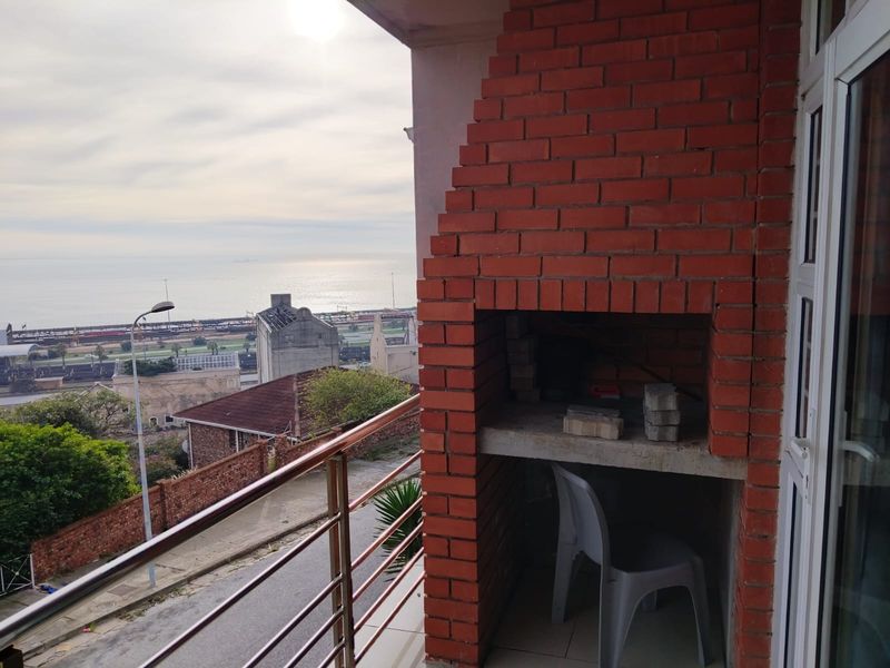 A balcony featuring a built-in brick braai, metal balustrade, and expansive coastal views, providing an ideal space for outdoor entertaining.