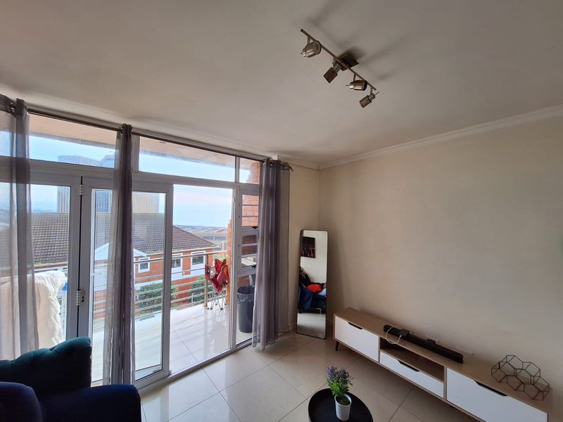 A bright living room featuring large sliding glass doors leading to a balcony, neutral tiled flooring, and modern track lighting.