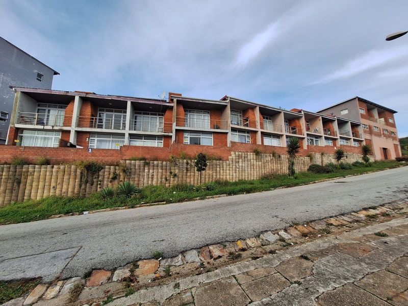 Exterior view of a multi-story apartment complex featuring brick facade, private balconies with metal railings, and a tiered retaining wall along the street.