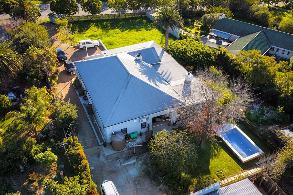 Aerial view of the property featuring a metal roof, swimming pool, and surrounding garden area with driveway access.